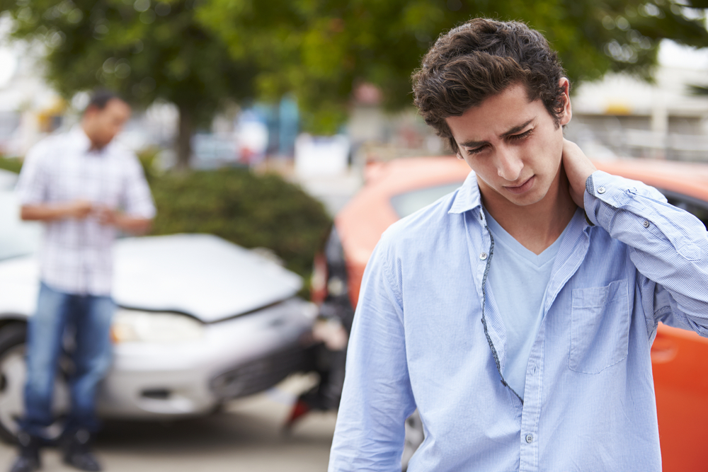 car accident lawyer with a man holding his neck standing in front of a recent car accident